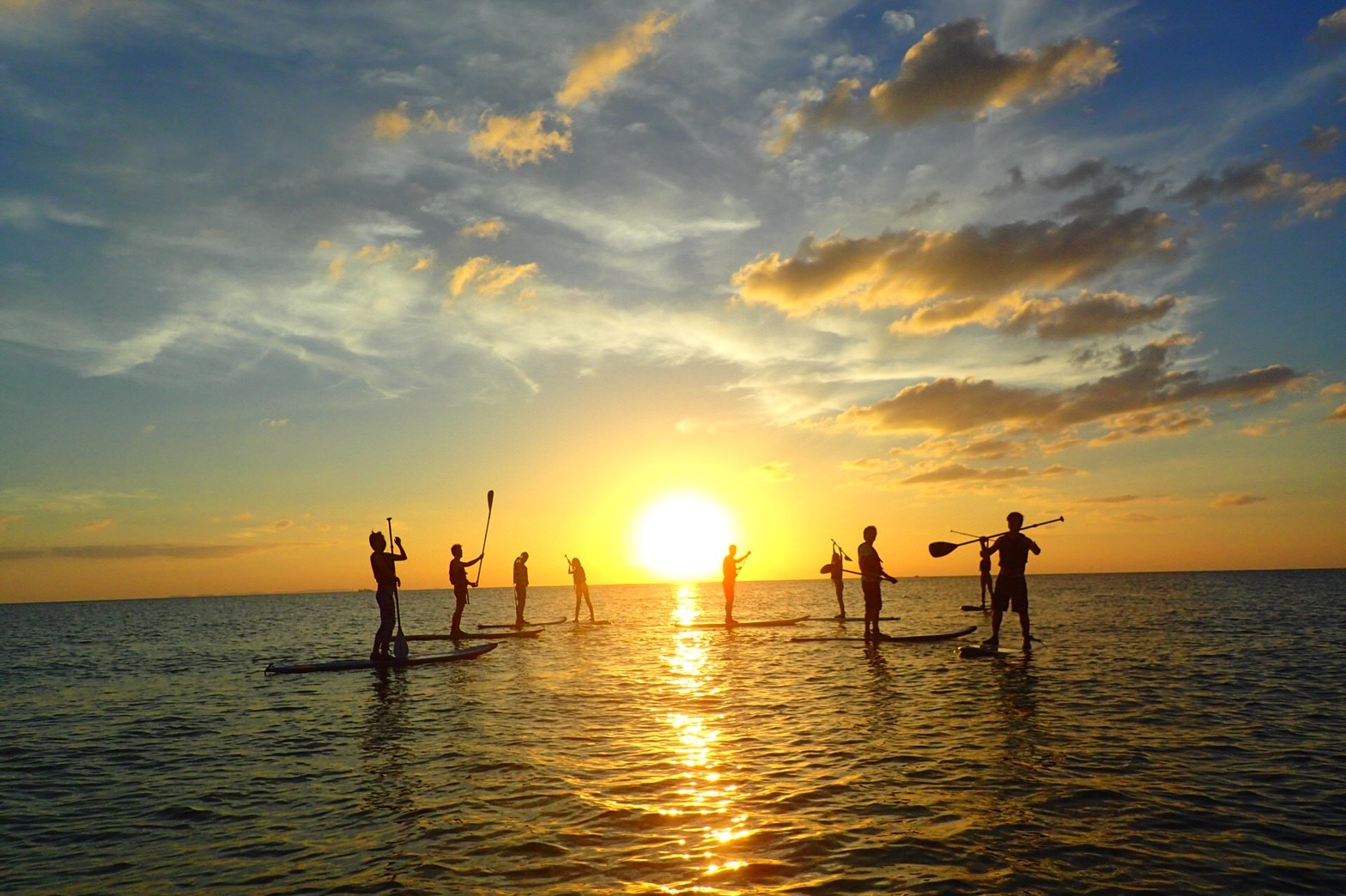 沖縄の読谷村の海で夕日の中SUPするグループ